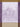 A rectangular tea towel featuring a purple and toile-style botanical pattern with an arched window motif and decorative border.