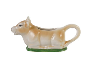 Cow shaped creamer laying on a bed of green grass