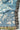 Wren Blanket – Fringe | Chambray. Birds sit among branches in this white on blue design. There is fringe around the edges alternating black/white and multicolored.