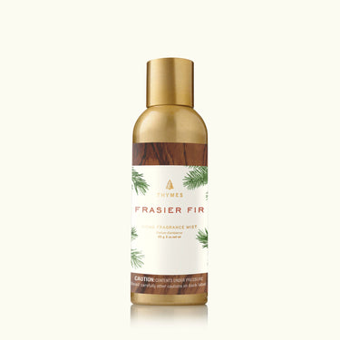 A bottle of Thymes Frasier Fir Home Fragrance Mist with a label showing the product name and a Frasier Fir tree. The bottle is transparent with a gold-colored cap and a white spray label.