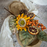 Decorative arrangement with sunflower, oranges, and leaves on a textured surface