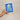 Hand holding a blue plantable seed paper envelope with white floral design on a beige background
