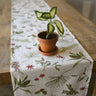 Rustic wood table featuring the berries and boughs linen table runner and a small potted plant. 