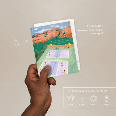 Hand holding a plantable seed paper envelope with illustrations of a birthday party scene on a beige background.