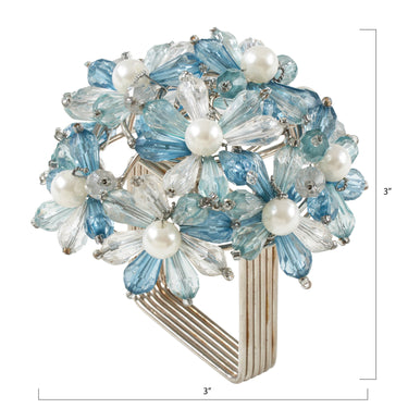 A floral-shaped napkin ring featuring light blue faceted glass petals, clear glass petals, and white faux pearls, mounted on a silver-toned multi-prong band. White dimension lines indicate a height and width of 3 inches.