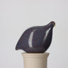 Decorative ceramic bird on a white pedestal against a light gray background