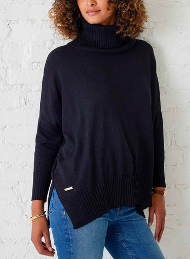Person wearing a black turtleneck sweater and blue jeans against a white brick wall.