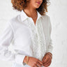 Close up image of the model wearing Tuxedo Ruffle shirt. The top button is unbuttoned, and she has her hands in front of her. She is wearing several gold colored bracelets.