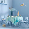 Dining table set with a light blue tablecloth, white chairs, and decorative items against a light blue wall.