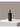 A black felt wine bottle carrier with a top handle, standing upright on a white platform against a warm gray background.