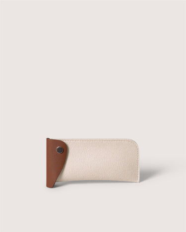 A minimalist card holder or wallet in cream-colored textured leather with a contrasting brown leather tab on the left side secured by a silver snap button, set against a solid light beige background.