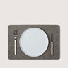 A rectangular gray felt placemat styled with a white ceramic plate, a silver fork, and a knife with light wood handles, set against a solid light beige background.