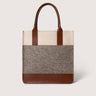 A structured tote bag with a color-blocked design featuring a cream top section, a brown felt middle section, and brown leather handles and base trim, shown against a light gray background.