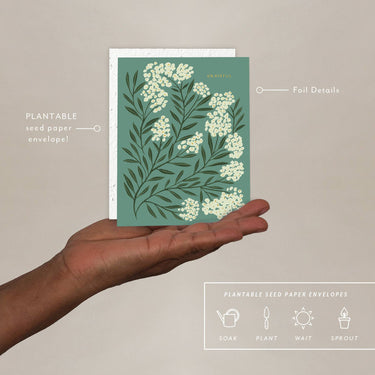 Hand holding a plantable seed paper envelope with floral design on a beige background