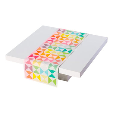 A multicolored geometric patterned table runner with origami-like folds, placed on a white table.