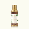 A bottle of Thymes Frasier Fir Home Fragrance Mist with a label showing the product name and a Frasier Fir tree. The bottle is transparent with a gold-colored cap and a white spray label.